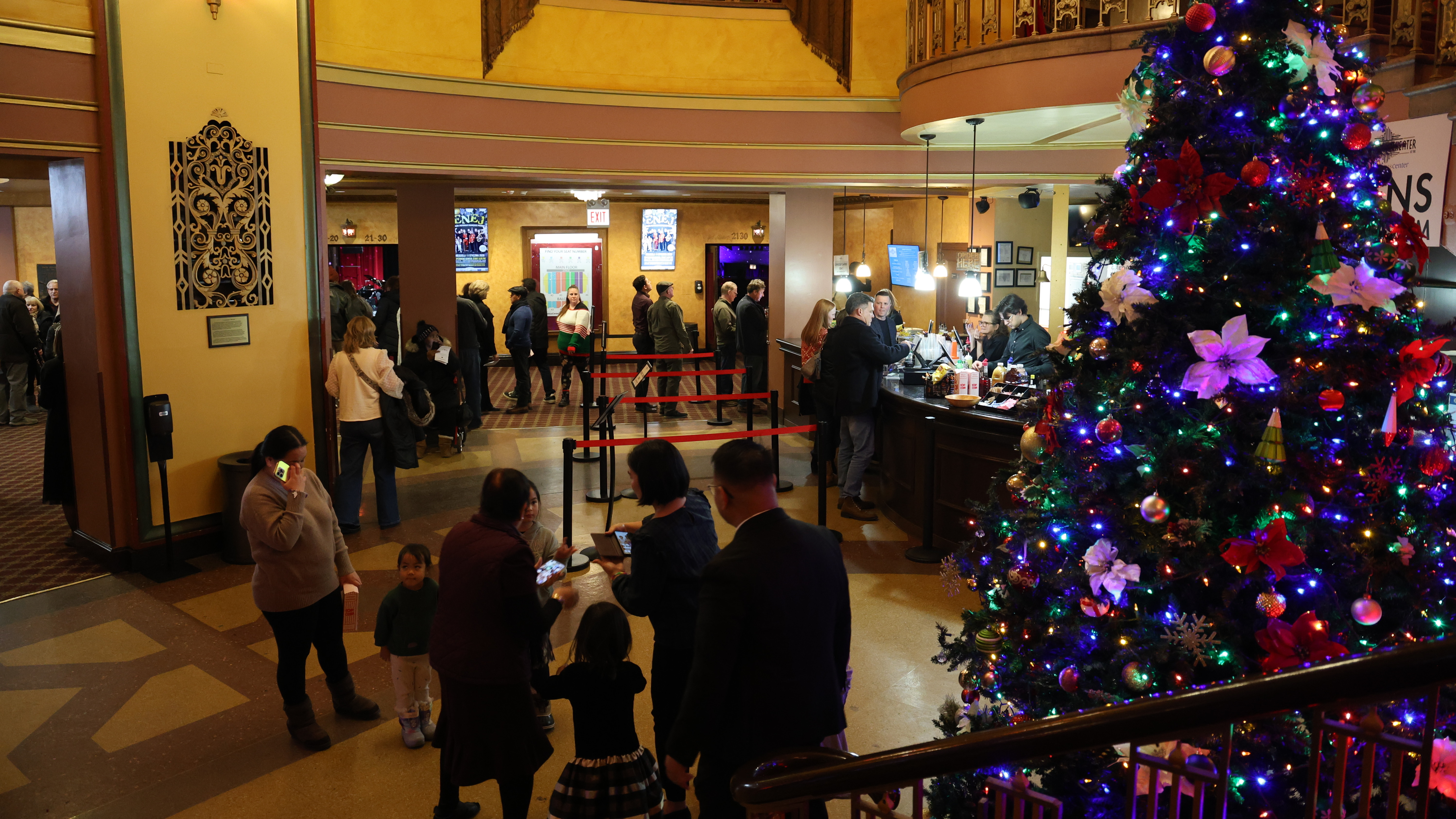 Ornate theater lobby with a Christmas tree and people.